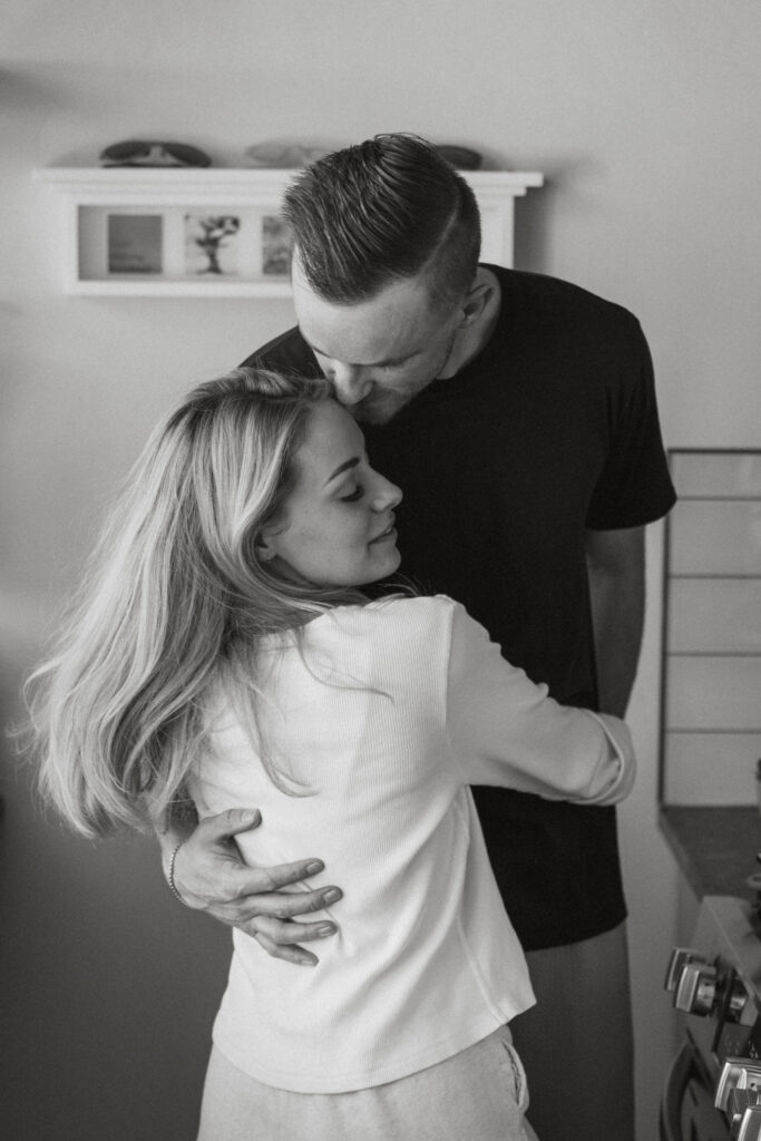The groom wrapping his arms around his wife and softly kissing her forehead 