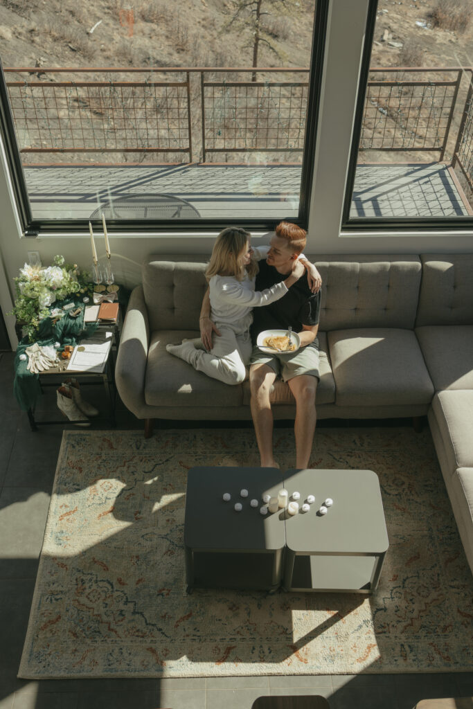 Bride snuggling up close with groom on couch as they share breakfast together