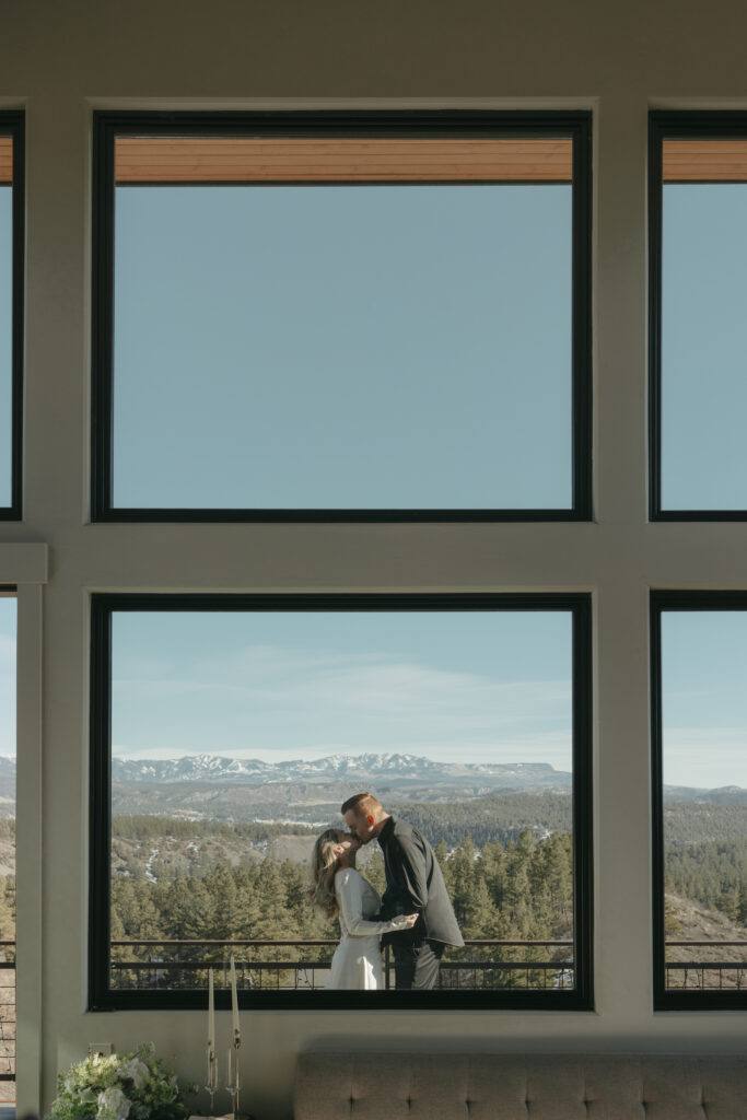 Bride and groom kissing as they stand on the balcony of their Airbnb overlooking the Colorado mountains 