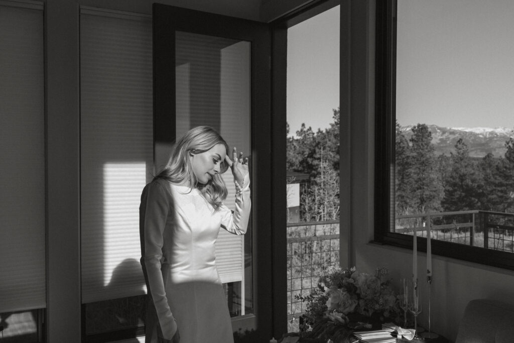 Bride pushing back her hair as she looks out the window towards the mountains 