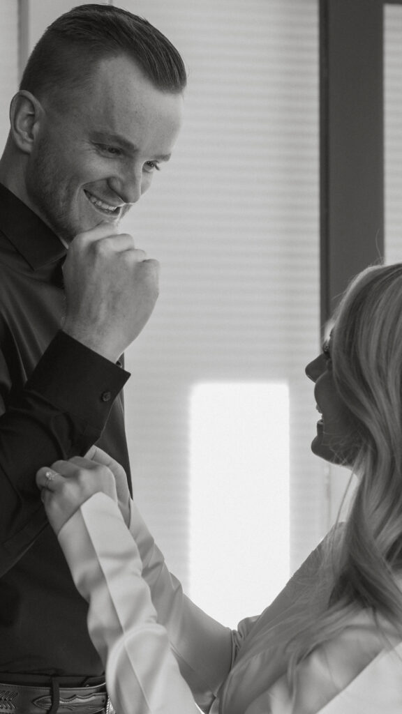 Groom smiling at his bride as she helps him secure his cufflinks