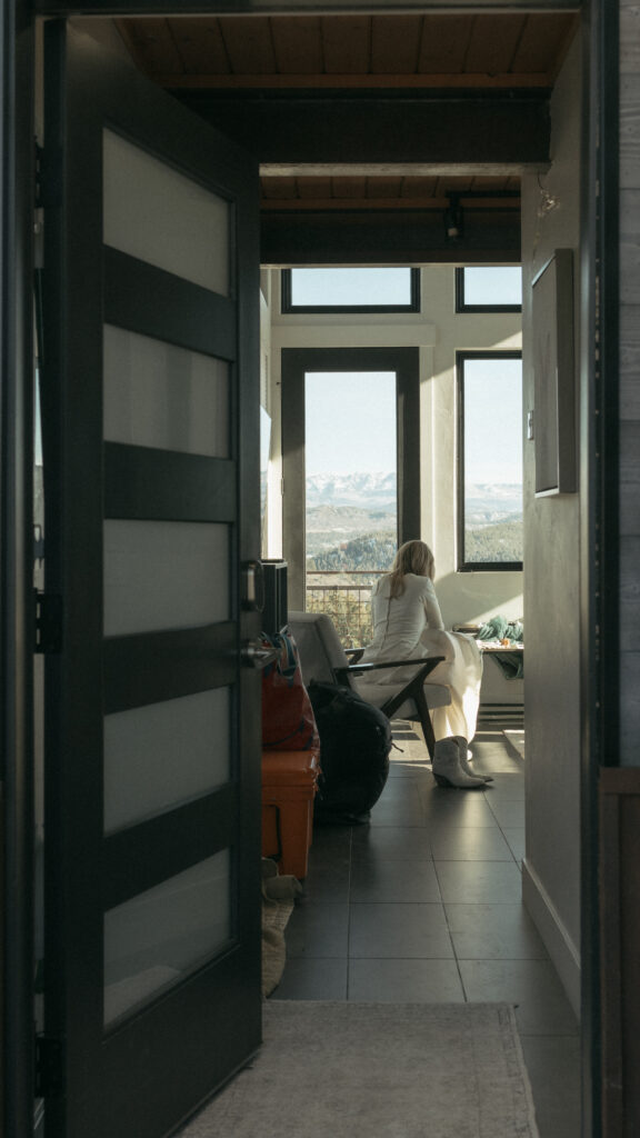 Bride sitting in the chair getting her shoes on, photographed in the doorway