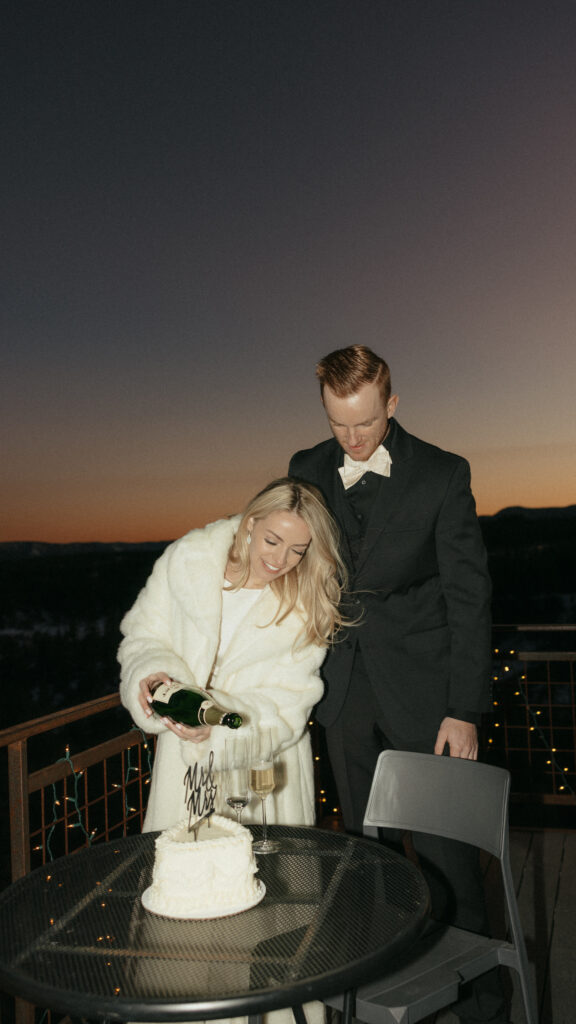 Bride pouring champagne into glasses with husband standing on balcony at sunset