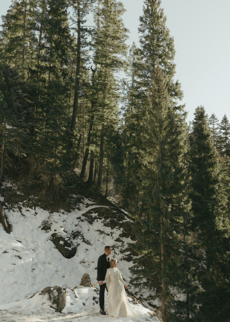 Bride and groom standing in the snow, overlooking the sunset in the mountains