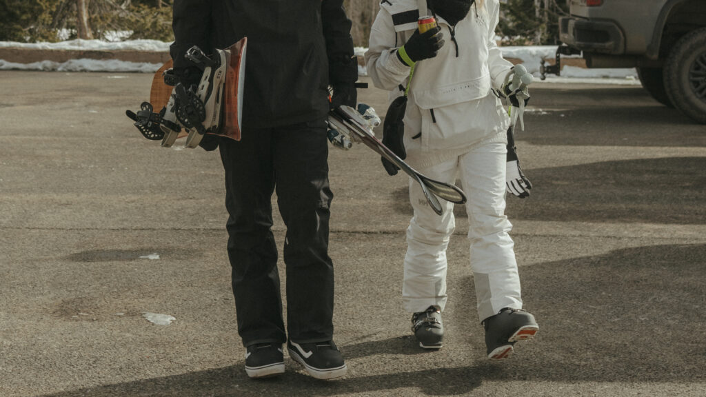 Bride and Groom holding their snowboard and skis as they walk towards the ski area on their elopement day