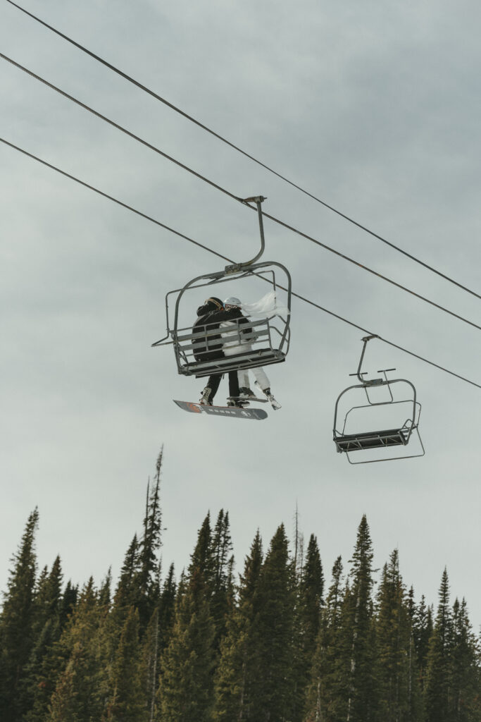 bride and groom on their elopement day riding the chair lift to the top of the mountain at Wolf Creek Ski Area, veil blowing in the wind