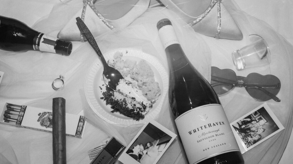 wedding detail flat lay with wine bottle, cake, rings, and accessories styled for reception