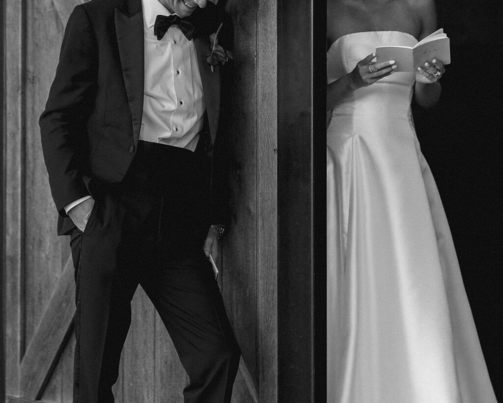 Close up of groom in tuxedo leaning against barn door during Trinity View Farm wedding