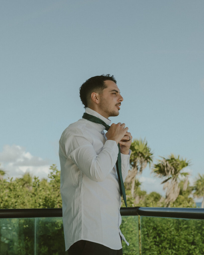 groom tying tie balcony ocean view destination wedding Mexico groom portrait tropical setting