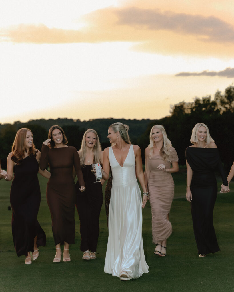 bride and bridesmaids walking together laughing at sunset