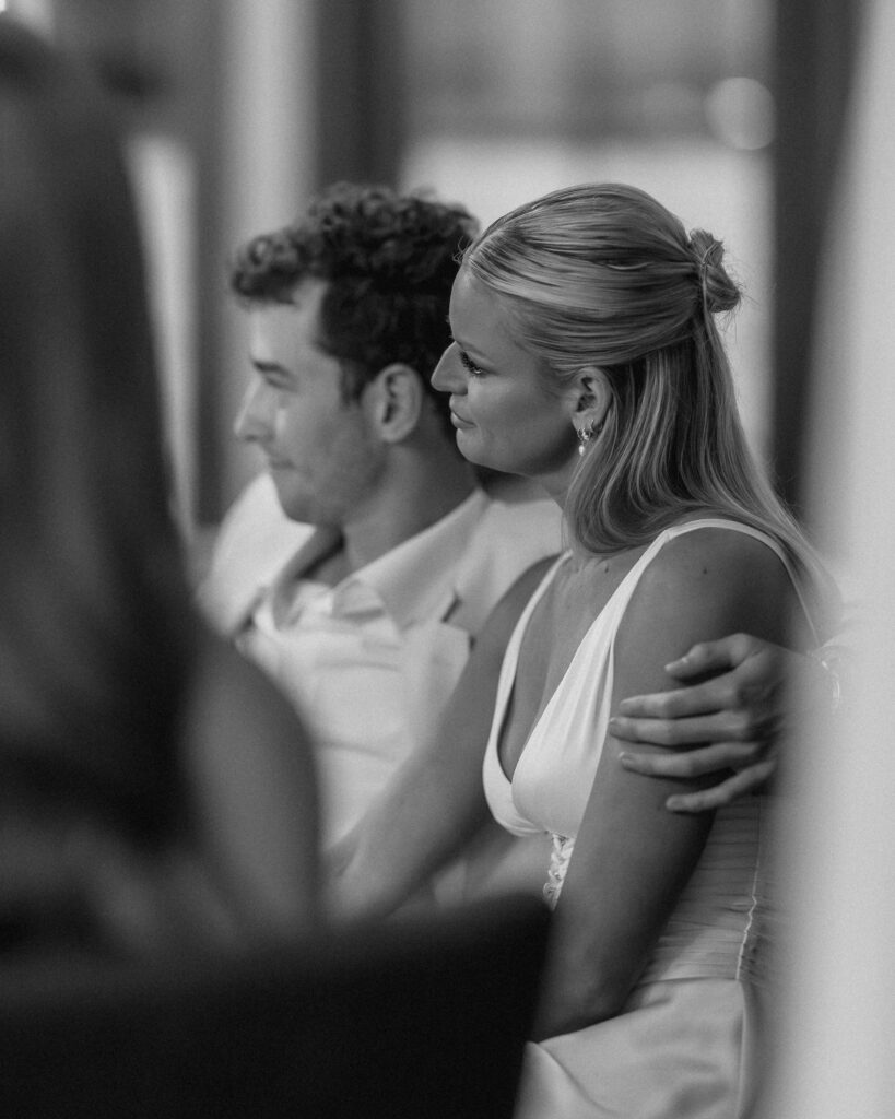 groom holding onto his bride smiling while they listen to speeches