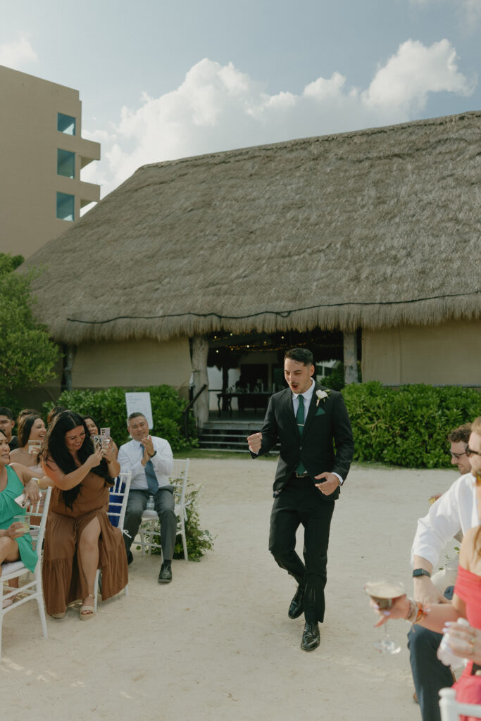 groom celebrating walking down aisle destination beach wedding Mexico candid joyful moment