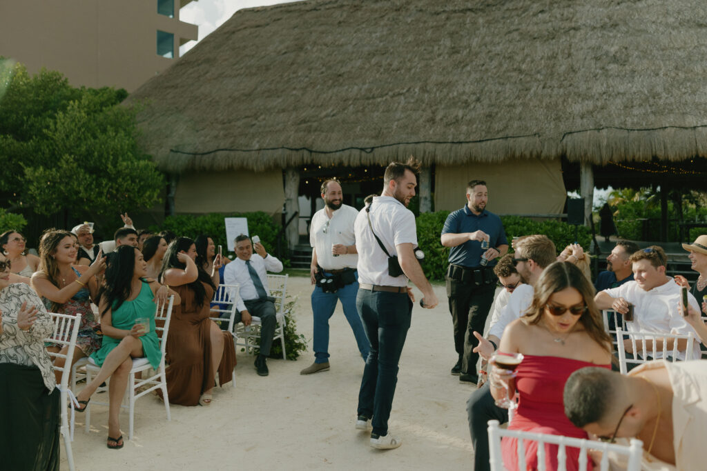 wedding guests celebrating passing drinks fun candid moment beach destination wedding Mexico
