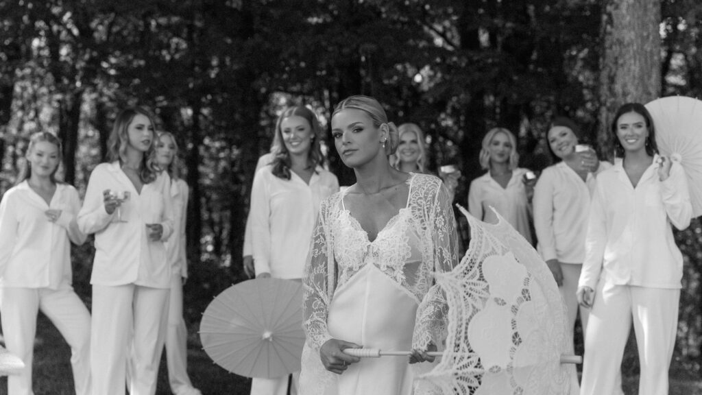 Bride with bridesmaids in white outfits holding parasols during cinematic Trinity View Farm wedding portraits