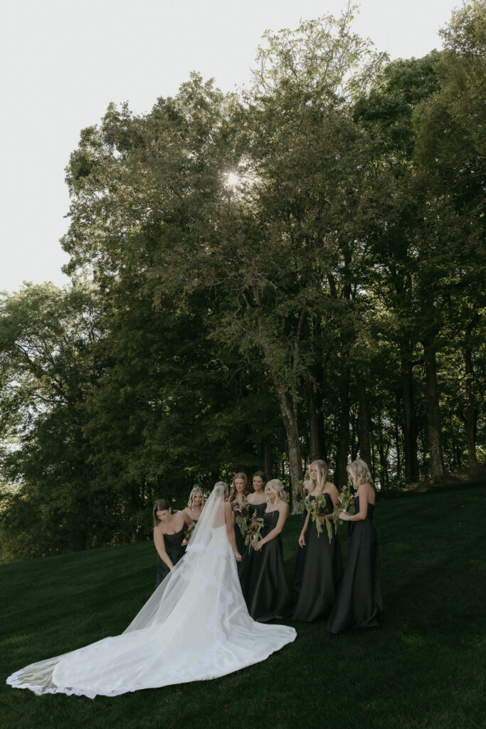Bride and bridesmaids in black dresses gathered on hillside during Franklin Tennessee wedding
