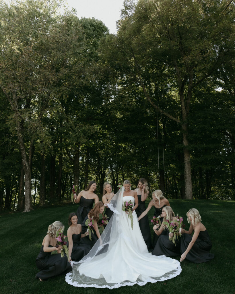 Bride surrounded by bridesmaids in black dresses holding bouquets at Trinity View Farm wedding