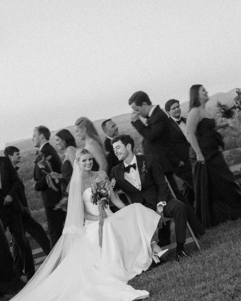 Bride and groom seated with wedding party moving around them during cinematic wedding moment in Franklin TN