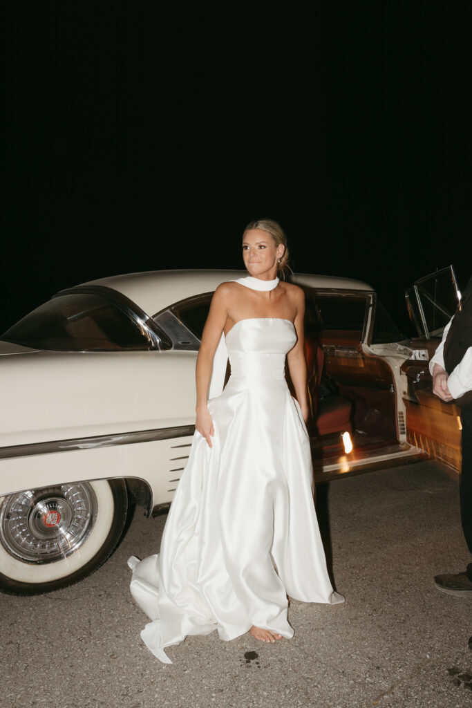 Bride standing beside vintage getaway car at night after wedding reception in Franklin Tennessee
