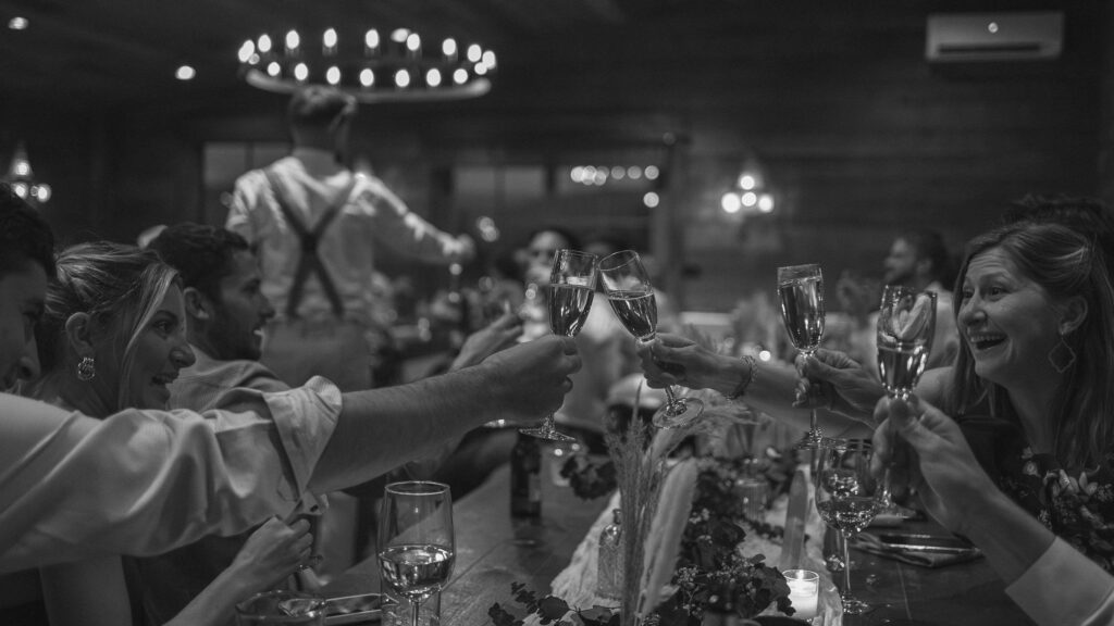 wedding reception toast with guests clinking glasses at candlelit table, candid celebration moment