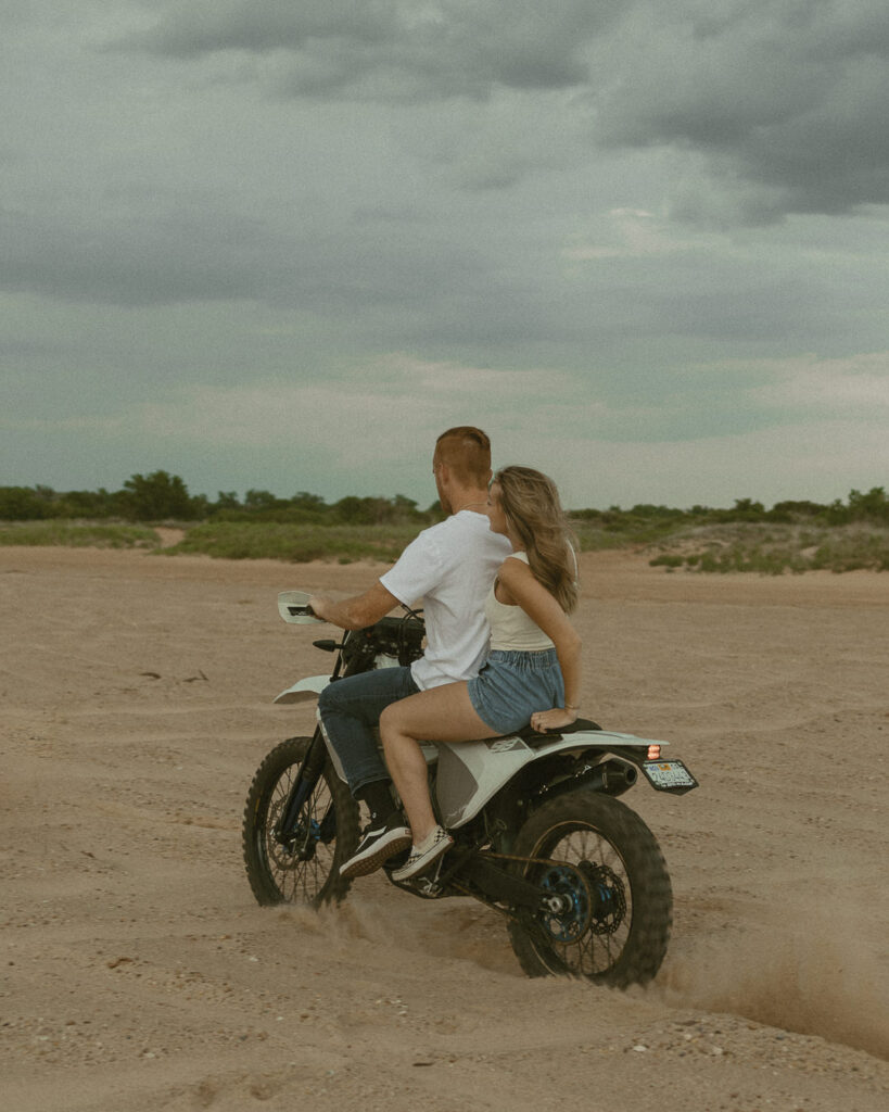 Couple riding a dirt bike through sand during an adventurous Texas engagement session