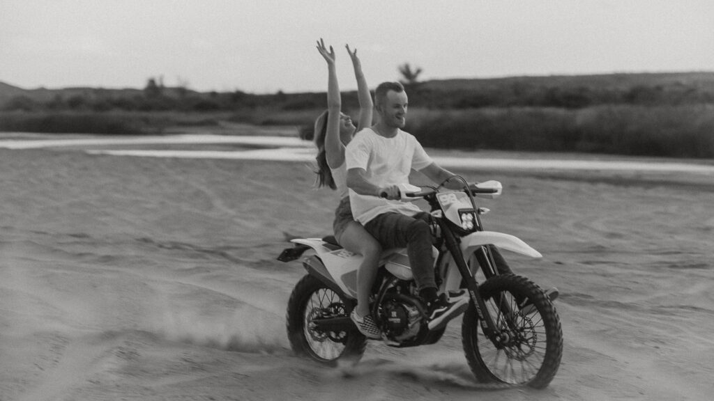 Couple riding motorcycle with arms outstretched in cinematic engagement session