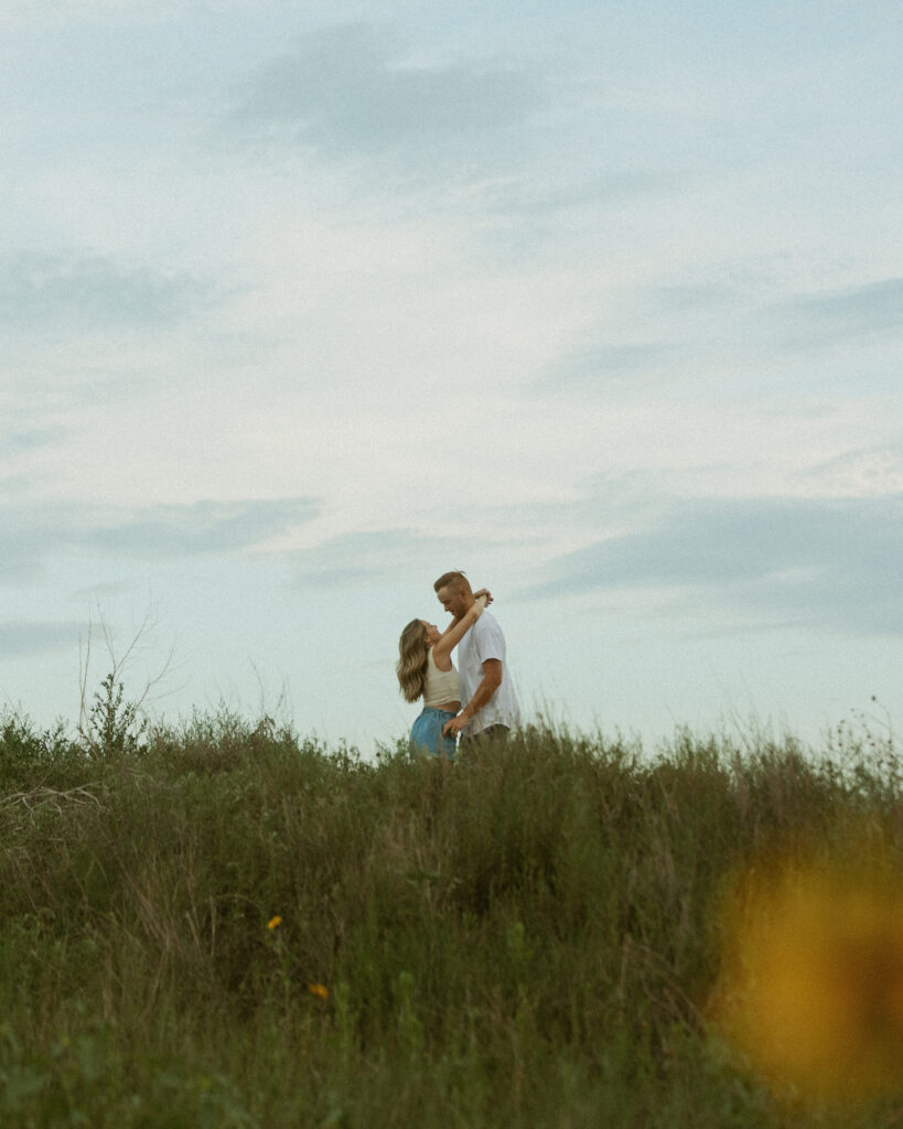 Wide cinematic engagement photo of couple in tall grass field at sunset in Texas