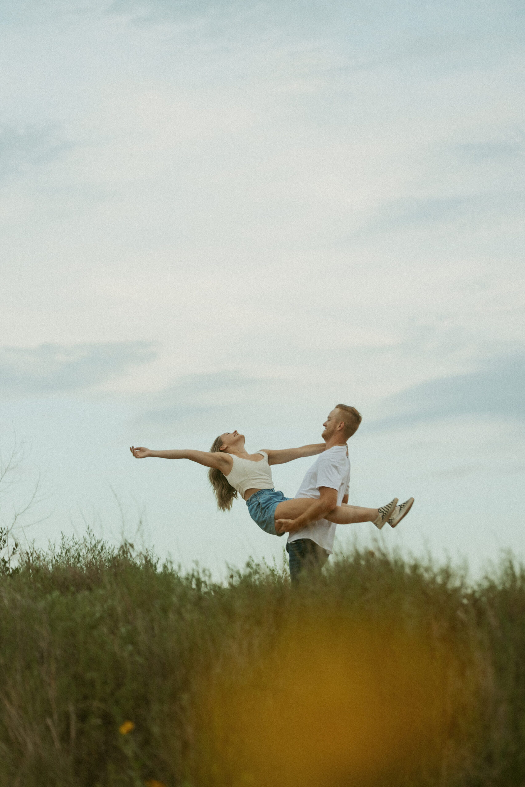 Couple dancing and spinning in tall grass during golden hour engagement session in Texas