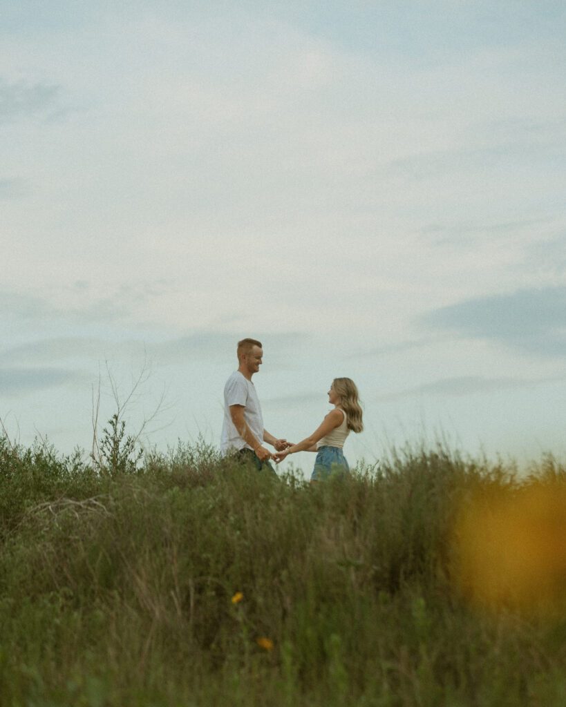 Playful engagement photo of couple holding hands and laughing in open field at sunset in Texas